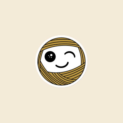 Wink, a winking mustard Yarn Creature magnet, 3 × 3 in, on a cream background