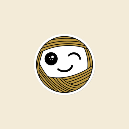 Wink, a winking mustard Yarn Creature sticker, 3 × 3 in, on a cream background